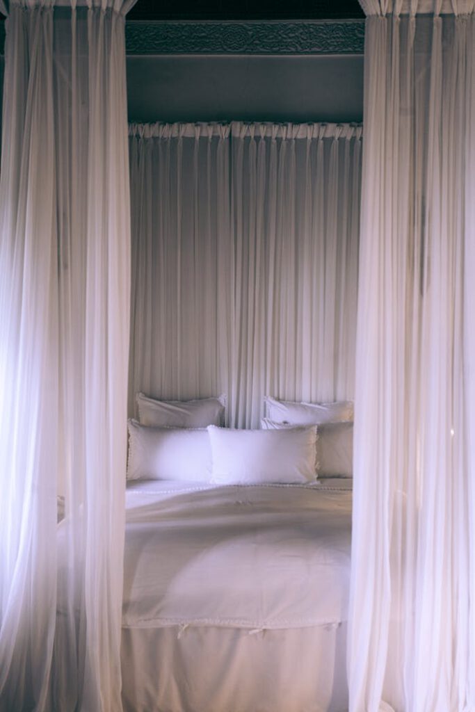pexels-photo-4916513 A cozy and serene canopy bed draped with translucent white curtains creating a tranquil bedroom setting.